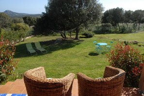 Eine Terrasse mit Korbstühlen, einem kleinen Tisch und einem Rasen.