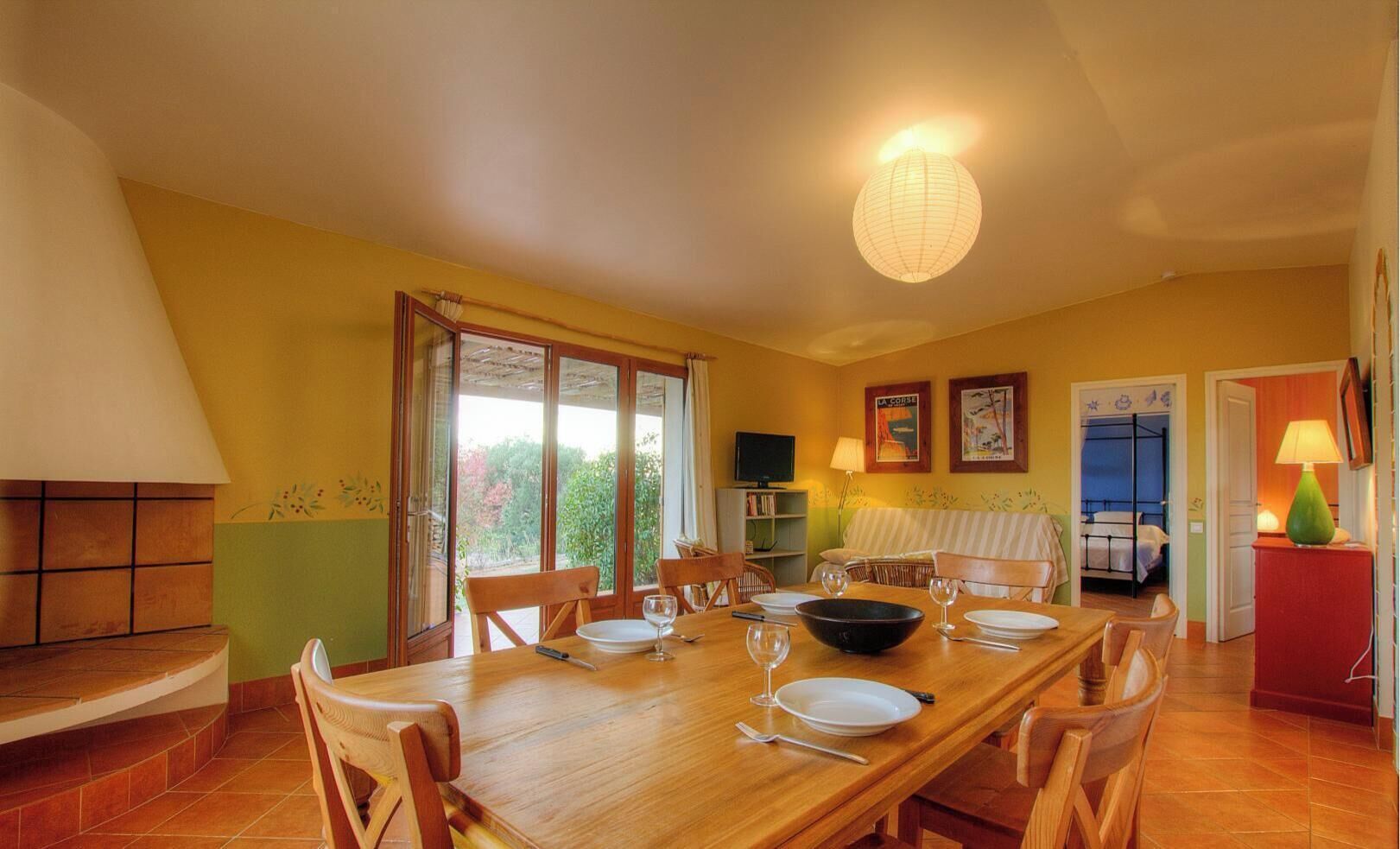A dining area with a wooden table set for four, a sofa, a TV, and a bed with a bunk.