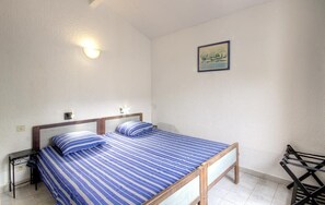 Ein Einzelbett mit Holzrahmen und einer blau gestreiften Bettdecke, ein Nachttisch mit Lampe sowie ein gerahmtes Bild an der Wand.