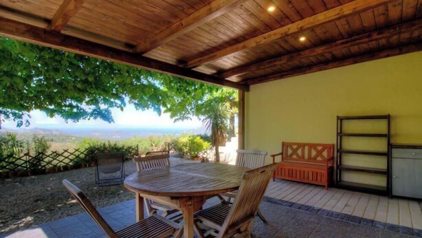 Eine Terrasse mit runder Holztisch und Stühlen, einer Holzbank und einem Fenster mit Metallrahmen.