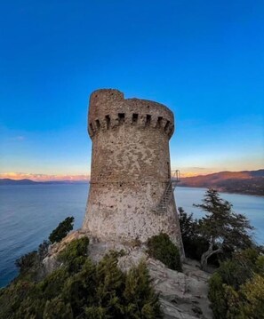 A historic stone tower with a crenellated top, overlooking a body of water and distant land. - Capu di Muro - COTI CHIAVARI (COTI CHIAVARI)