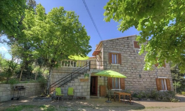 A stone building with a staircase, outdoor seating, and a green umbrella. - Le 19801 - PETRETO BICCHISANO (PETRETO BICCHISANO)
