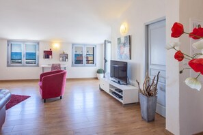 Un salon moderne dotĂ© dâun tĂ©lĂ©viseur, de siĂšges, dâune vue sur la mer et dâune porte ornĂ©e de tulipes rouges.