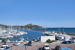 Un port de plaisance avec des bateaux amarrés, un parking avec des voitures et, au loin, un paysage vallonné.