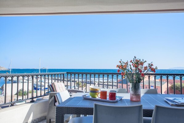 Un balcon avec vue sur la mer, une table avec des boissons et un vase de fleurs.