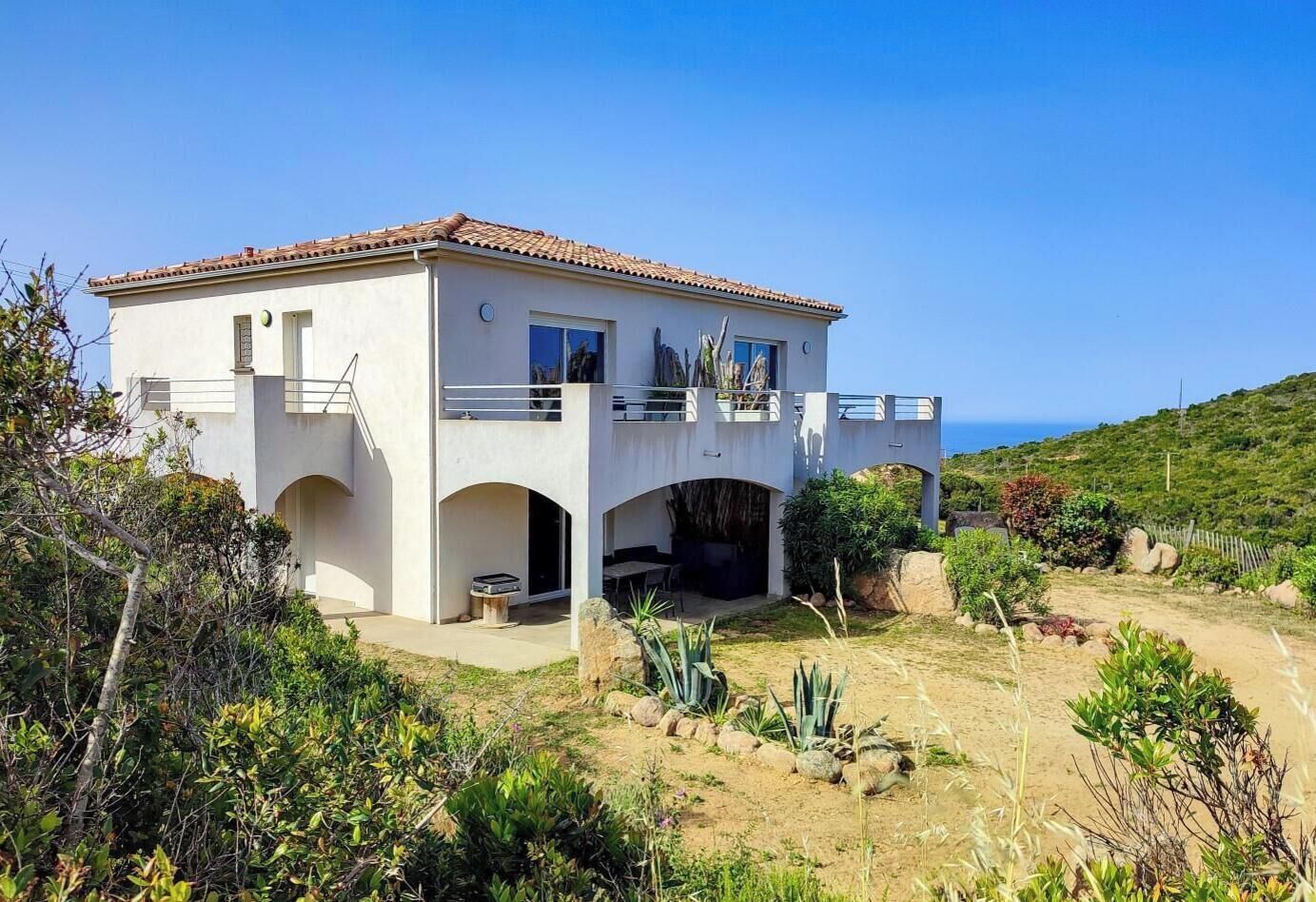 Una casa de dos pisos con un balcón, un patio y vista al mar.