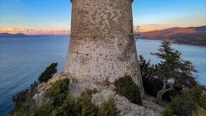 Ein historischer SteinTurm mit Zinnen, der auf ein Gewässer und ferne Land blickt.