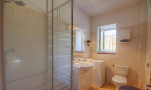 Un baño con cabina de ducha de vidrio, lavabo, inodoro y ventana.