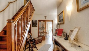 Eine Holztreppe führt zu einem Essbereich, an der Wand ist ein Kreuz, ein gerahmtes Bild und ein Schwarzes Brett mit Aushängen.