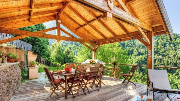 A wooden deck with a table and chairs, surrounded by greenery and a mountainous backdrop. - A Sicareccia - PIAZZOLE (PIAZZOLE)