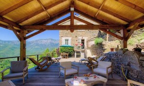 Una terraza de madera con mobiliario exterior, un muro de piedra y vistas a la montaña.