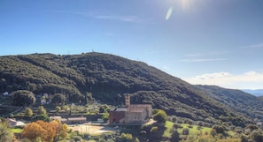 Ländliche Landschaft mit einem markanten Hügel, einem kleinen Gebäude mit Glockenturm und verstreuten Häusern.