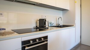 Una cocina moderna con armarios blancos, encimera negra, horno integrado, cafetera y lavabo.