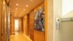 Pasillo de hotel con piso de madera, puerta de cristal y un cuadro abstracto colorido, además de un portero automático en la pared.