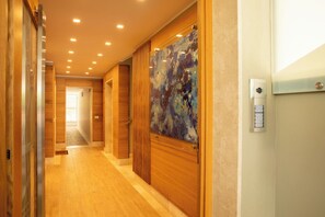 A hotel corridor with wooden flooring, a glass door with a colorful abstract painting, and a wall-mounted intercom. - C&B House-Relax & Sea (Alghero)
