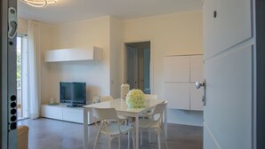 Una habitación moderna con televisión de pantalla plana, una mesa de comedor con sillas y un armario blanco.