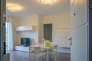 A modern room with a flat-screen TV, a dining table with chairs, and a white cabinet. - C&B House-Relax & Sea (Alghero)