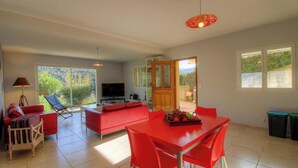 Un'ampia zona giorno con un divano rosso, un tavolo da pranzo con sedie rosse, una TV e un'ampia finestra con vista su spazi verdi.