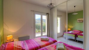 Camera da letto con due letti, un'ampia finestra e vista sul verde.