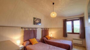 Une chambre avec deux lits, une petite table de chevet, un luminaire suspendu, une fenêtre avec des rideaux et un climatiseur fixé au mur.