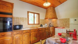 Une cuisine avec des meubles de rangement en bois, une cuisinière, un four à micro-ondes et une fenêtre.