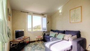 A room with a sofa, a TV on a stand, a small table, and a window with curtains. - I Pinzzelli 2 - FARINOLE (FARINOLE)