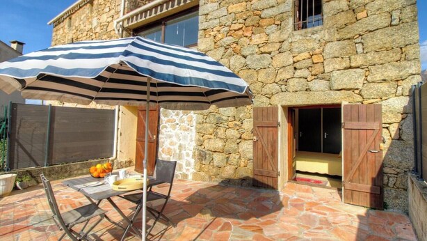Un edificio de piedra con un patio que tiene una mesa, sillas y un paraguas a rayas.