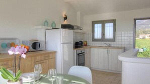 Cocina compacta con microondas, tostadora y lavabo. Hay una mesa de comedor con sillas y un florero.