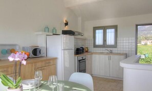 Eine kompakte Küche mit Mikrowelle, Toaster und Spüle. Ein Esstisch mit Stühlen und eine Blumenvase sind ebenfalls vorhanden.