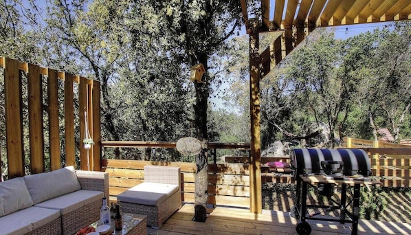 Eine Holzterrasse mit Grill, einer Sitzecke und einer hängenden Leuchte.