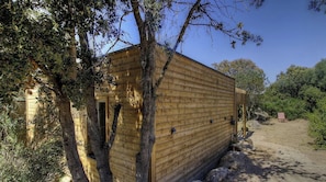 Eine Holzhütte mit Fenster und Tür, umgeben von Bäumen und einem Feldweg.