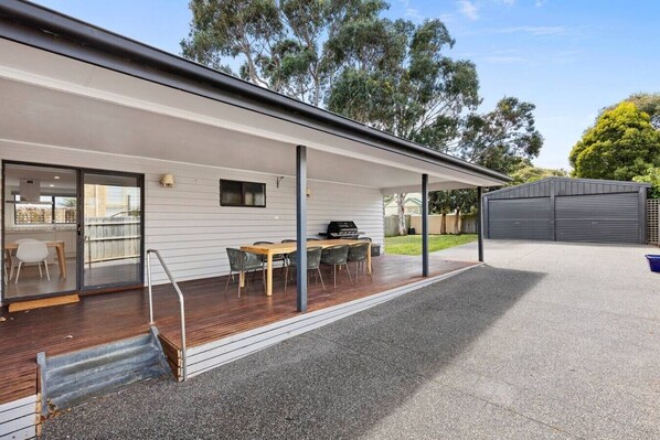 A covered patio with a wooden table and chairs, a grill, and a garage.