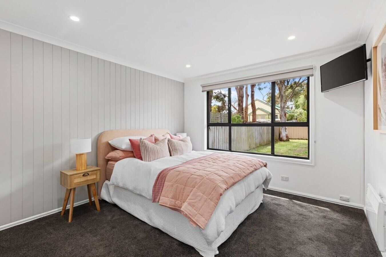 A bedroom with a bed, bedside table, lamp, window, and TV.