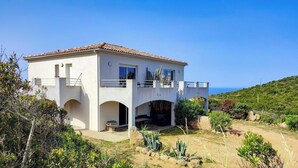 Uma casa de dois andares com varanda, área de pátio e vista para o mar.