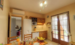 A compact kitchen with a refrigerator, microwave, and sink. There is a dining table with chairs and a basket of fruit. - L'alivetu - PERI - Gîte (PERI)