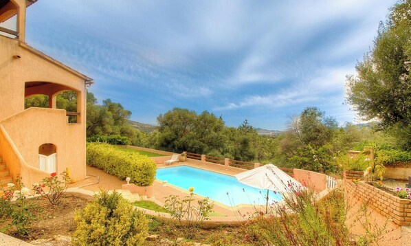 A swimming pool with a view of the countryside, a covered patio, and a building with a unique architectural design. - L'alivetu - PERI - Gîte (PERI)