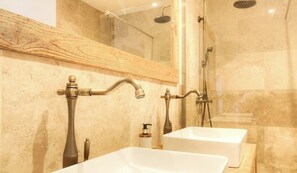 Un baño con tocador de madera, dos lavamanos, un espejo y una ducha con mampara de vidrio.