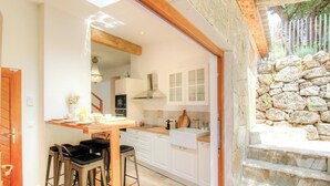 Cozinha com armários brancos, uma mesa de madeira e uma parede de pedra.