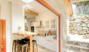 Una cocina con armarios blancos, una mesa de madera y una pared de piedra.