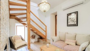 Um quarto estilo loft com vigas de madeira aparentes, escada, conjunto de sofás, poltrona, candelabro e quadro na parede.
