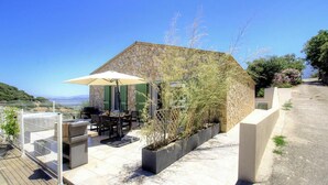 Un bâtiment en pierre doté d’une terrasse, de mobilier d’extérieur et offrant une vue sur la mer.