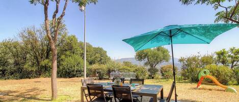 An outdoor dining area with a table and chairs, a large umbrella, and a playground structure.