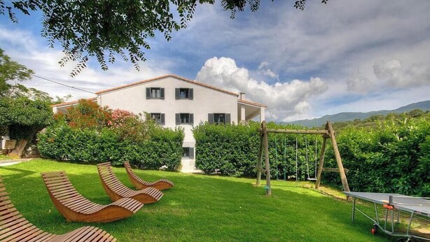 A two-story building with a white facade, a wooden deck with lounge chairs, and a swing set in a well-maintained garden. - CAPANELLA - SERRA DI FERRO (SERRA DI FERRO)