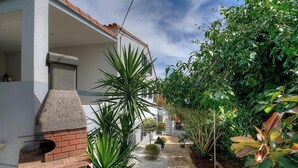 A narrow pathway leading to a house with a brick fireplace, surrounded by lush greenery and a white building with a red-tiled roof. - CAPANELLA - SERRA DI FERRO (SERRA DI FERRO)
