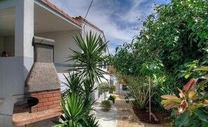 A narrow pathway leading to a house with a brick fireplace, surrounded by lush greenery and a white building with a red-tiled roof. - CAPANELLA - SERRA DI FERRO (SERRA DI FERRO)