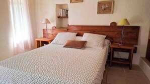 Een slaapkamer met een bed, twee nachtkastjes, een wandplank met boeken en een lamp.