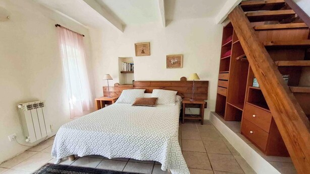Een slaapkamer met een bed, een houten hoofdbord, nachtkastjes, een radiator en een houten trap.