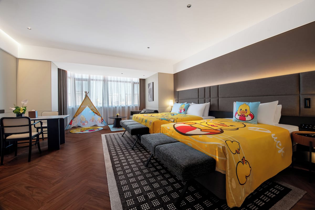 Habitación de hotel con una cama grande, un escritorio, una silla, una mesita y una tienda de campaña, además de una ventana con cortinas.
