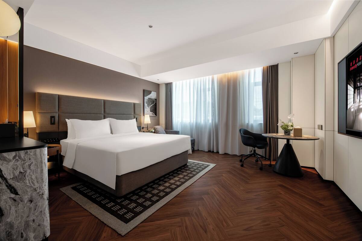 Una habitación de hotel moderna con una cama grande, un escritorio, una silla y un televisor.