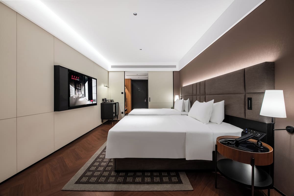 Habitación de hotel con una cama grande, un escritorio con lámpara, un televisor montado en la pared y una puerta que da a otra habitación.